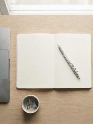 Overhead flat-lay of a minimalist desk setup, a mechanical pencil resting on a clean open notebook, silver laptop edge visible, bright diffused natural light, soft shadows, desaturated tones with a subtle blue accent, 35mm
