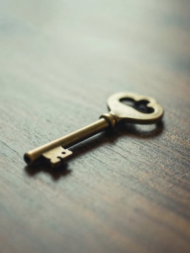Medium close-up of a heavy brass key resting on a polished dark wood surface, soft natural morning light, shallow depth of field. Muted forest green and cream tones.