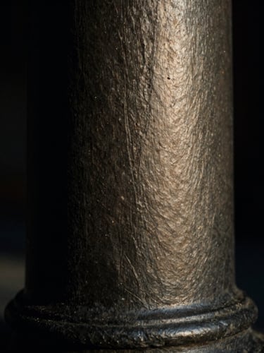Macro close-up of a dark slate architectural column in low-key dramatic chiaroscuro lighting, brushed metal texture, 35mm film.