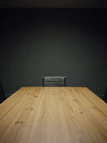Dark moody editorial photography of a quiet executive boardroom, low-key dramatic chiaroscuro lighting, deep charcoal and champagne gold tones, 35mm film.
