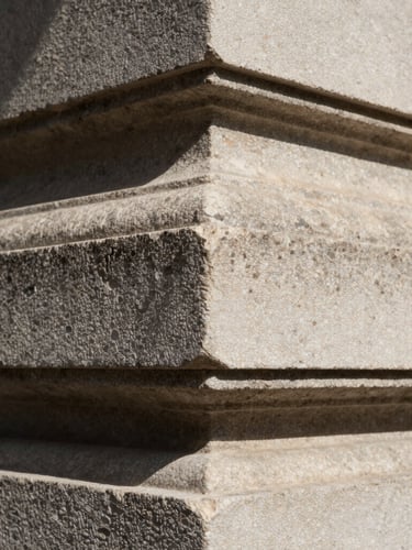 Tight macro crop of textured limestone architectural facade under sharp directional sunlight, high-contrast shadows.