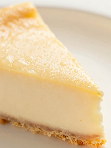 Macro shot of fresh cheesecake texture with soft condensation, warm side lighting, elegant linen background, shallow depth of field.