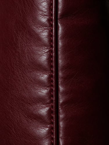 Extreme close-up of immaculate stitching on deep burgundy polished leather, side light highlighting the rich texture and grain, dramatic editorial style