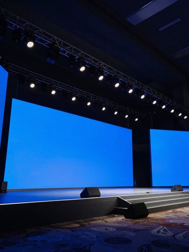Dramatic wide-angle shot of a large corporate stage with sharp blue LED screens and professional lighting rigs, deep shadows, high-contrast