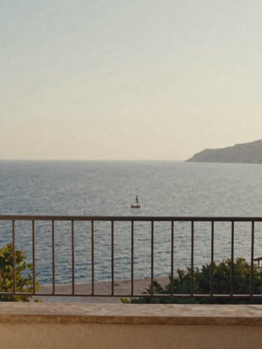 An empty private balcony overlooking a quiet Mediterranean bay at golden hour, soft warm light, elegant linen curtains blowing gently, 35mm film look