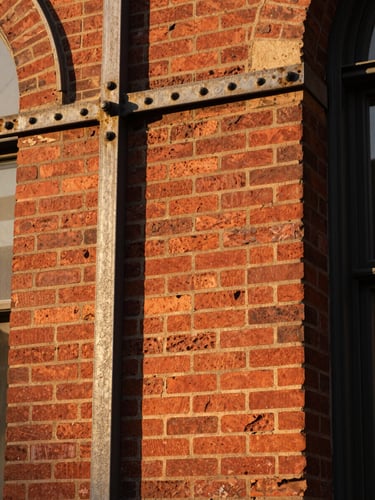 Close-up of historic St. Louis red brick masonry and weathered iron framing under warm golden hour light, showing solid architectural textures.