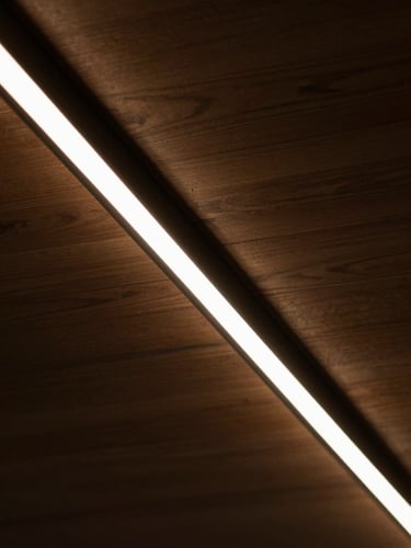 Close-up of a perfectly installed linear LED light channel in a dark wood ceiling, sharp architectural lines, warm amber glow, high-contrast shadows