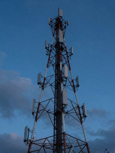 Wide-angle portrait shot of a telecommunication tower cutting through a dramatic, deep twilight sky, sharp architectural steel, cool blue tones.