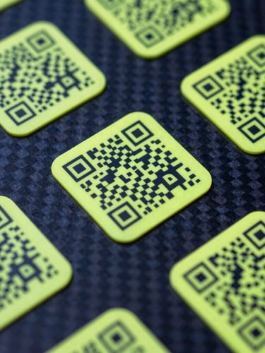 Premium physical QR tags on a carbon fiber surface, high-contrast studio lighting, sharp neon yellow edge-glow, macro 35mm focus