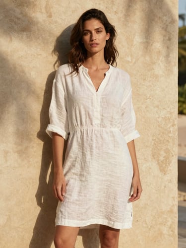 A woman in a white linen dress standing against a rustic textured plaster wall, warm sunlight, soft shadows, editorial fashion photography, 35mm.