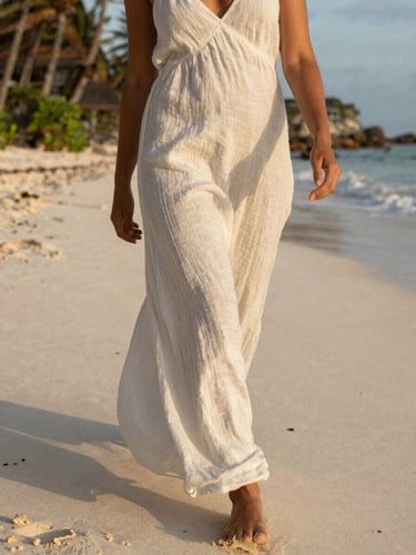 A close-up of a woman in a flowing white linen dress walking on a quiet, sun-drenched Tulum beach during golden hour, soft shadows, 35mm.