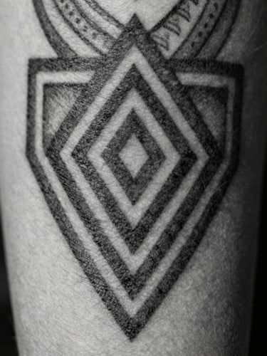 Extreme macro shot of a fresh black ink tattoo on skin, showing sharp geometric patterns and deep chiaroscuro lighting, high contrast, black and white.