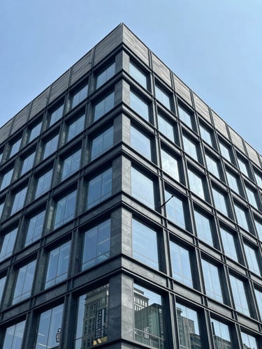 Wide architectural angle of a modern commercial office building facade under crisp daylight, cool blue slate tones, sharp structural steel lines