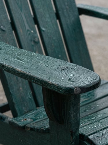 Close-up of textured resin and weathered wood grain on an Adirondack chair arm, water droplets beaded on the surface, overcast daylight