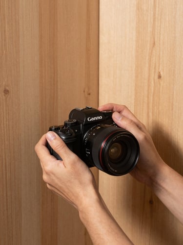 A close-up of hands holding a high-end camera, framing a beautifully finished pine wood wall corner with soft shadows