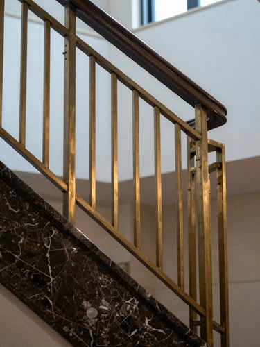 Architectural detail shot of a luxury hotel staircase railing in brushed brass and dark marble, cool natural light from above, no people, tight geometric framing emphasising craftsmanship of materials