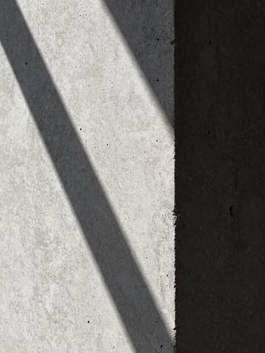 Extreme close-up of board-formed concrete texture under harsh midday sun, casting deep, sharp-edged architectural shadows.