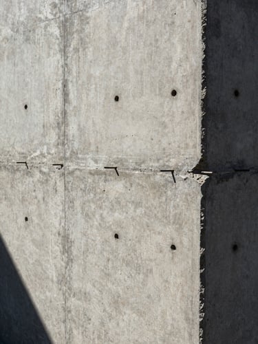 Extreme close-up of curing concrete wall with visible formwork tie holes, high-contrast shadows under harsh Baja sun.