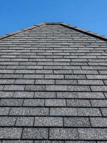 Close-up architectural shot of high-contrast charcoal architectural shingles, clean lines, bright desert sunlight, sharp shadows.