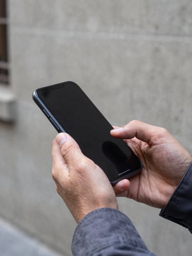 Close-up of hands holding a modern smartphone mid-use on a Santiago street, natural daylight, concrete urban wall in background, fingers scrolling the screen, sleeve of a work jacket visible