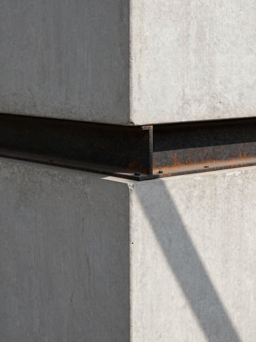 Fotografia arquitetônica em perspectiva de um ponto. Detalhe minimalista de uma quina de concreto aparente cinza claro encontrando uma viga de aço escovado escuro. Luz solar geométrica direta projetando sombras lineares nítidas. Sem pessoas.