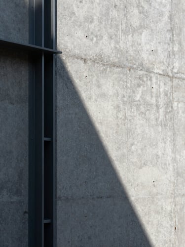 Vertical close-up of a raw concrete wall intersecting with a dark steel frame, sharp geometric sunlight casting a diagonal shadow, strict one-point perspective