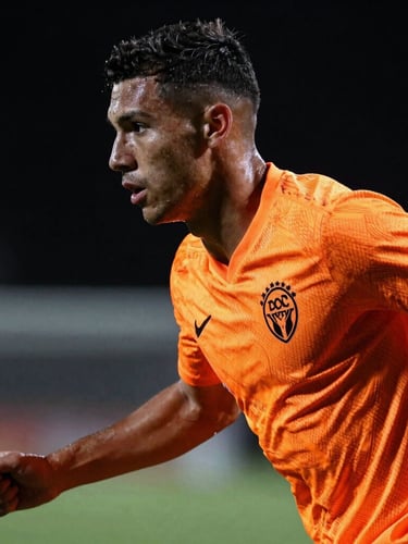 Dynamic sports photography, close-up profile of a determined football player wearing a vibrant neon orange technical jersey, dramatic lighting, dark background, 35mm lens
