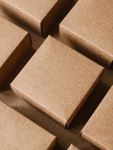 Overhead flat-lay of structured gift boxes in desaturated saffron and clay tones, soft natural side-light highlighting heavy-milled paper texture, 35mm film.