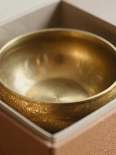 Macro close-up of a heavy-milled brass incense bowl resting inside a desaturated saffron-colored structured paper box, soft natural side-light, fine paper texture visible.