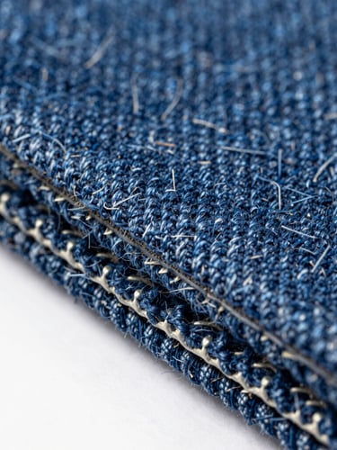 Extreme macro studio photograph of a dense indigo denim-fiber composite panel edge, showing compressed blue threads and structural binder matrix, crisp directional lighting, 35mm.