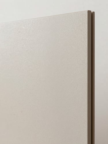 Extreme close-up of a pale ash decorative board surface under north-facing studio daylight, grain running diagonally, edge of the panel visible at right, cool off-white backdrop, no warming filter, material texture rendered at true scale