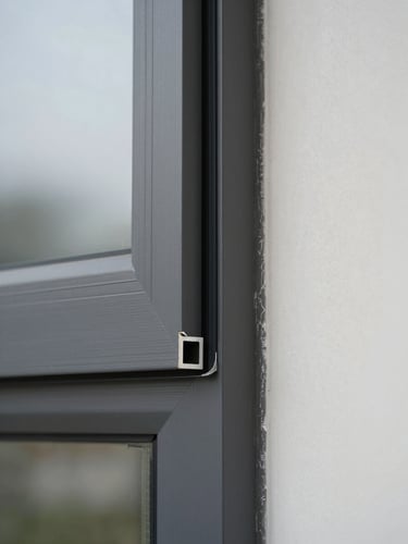 Extreme close-up of a precision-cut aluminum window frame corner installed on a real building facade, overcast daylight revealing the sharp mitered joint and tight rubber gasket seal, steel-gray profile against pale rendered wall, no people, no lifestyle styling