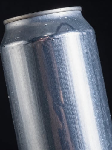 Macro close-up of a custom printed aluminum can showing tactile ink textures and crisp metallic silver details, dramatic high-contrast studio lighting catching metallic reflections, deep black background, cinematic 21:9 framing.