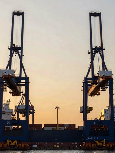 Wide architectural shot of a modern deepwater shipping terminal at sunset, cargo cranes framed symmetrically against a golden sky, high contrast, elegant corporate photography, 35mm.