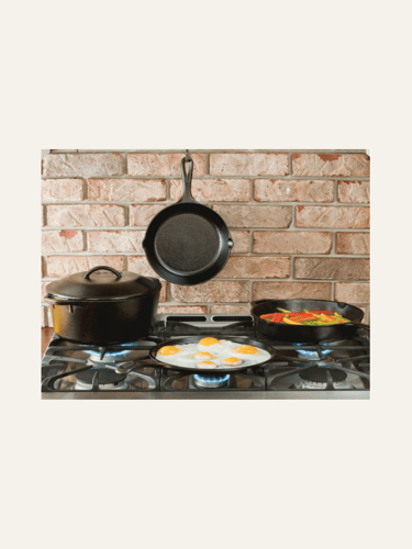 pciture of black Lodge 12 inch cast iron skillet on the back brick wall of a kitchen, behind a stove