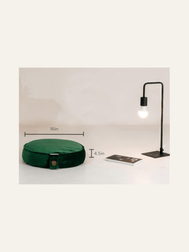 a picture of an emerald green round meditation cushion on a floor with a lamp beside it