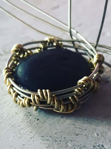 Colgante de joyería hecho a mano con alambre engarzado, que presenta una piedra oscura engastada