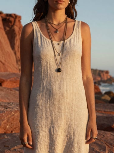 Medium environmental shot of a woman in a simple linen dress wearing multiple layered Dos Manos necklaces and rings, standing against the dramatic red cliffs of Baja California Sur, golden hour.