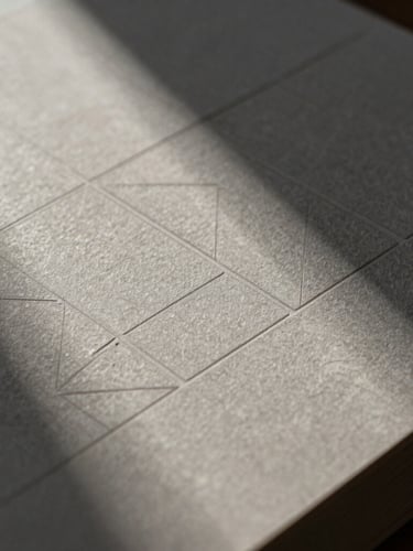 Extreme close-up of heavy stone-gray paper stock with embossed geometric grid lines, sharp directional side-light creating deep shadows, focusing on tactile texture.