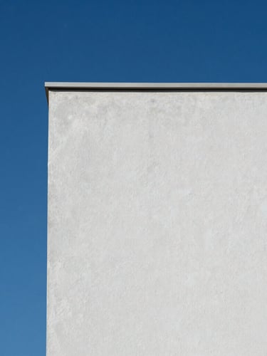 Minimalist close-up of a clean painted exterior wall texture against a deep blue sky, showing perfect matte finish and crisp architectural shadow.