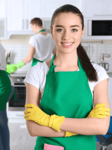 a woman in a green apron and gloves holding a cleaning sponge
