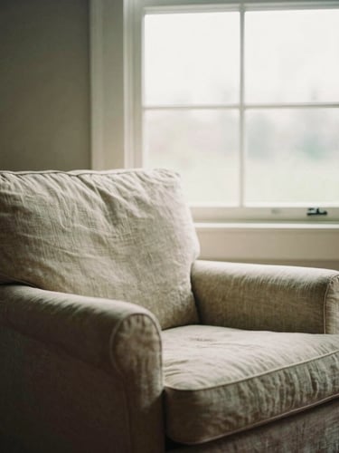 A comfortable linen armchair next to a tall window with soft light filtering through, domestic therapy space, 35mm film