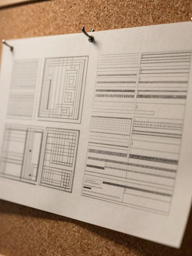Extreme close-up of custom-drafted paper patterns pinned to a corkboard, warm directional studio key light highlighting graphite lines and heavy paper texture.