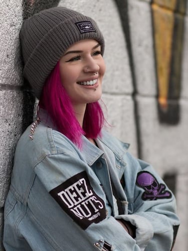 Mujer sonriente con el pelo rosa brillante, gorro gris y chaqueta