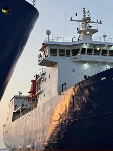 Sharp industrial photography of a massive offshore vessel docked at golden hour, cool LED work lights reflecting on the dark steel hull, architectural framing with negative space on the left.