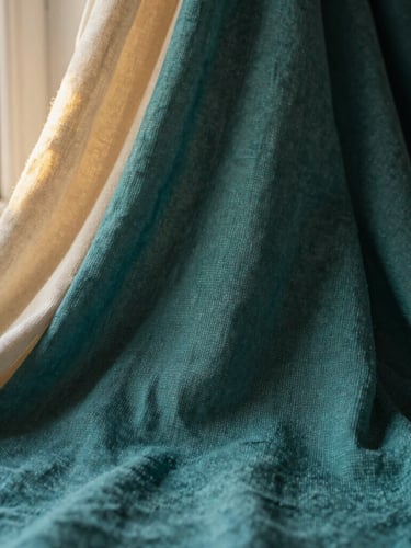 Close-up of finely woven mul cotton fabric, soft folds, light passing through, warm editorial photography, soft golden-hour window light, rich teal and ivory tones, shallow depth of field, 35mm, bleeding to the left edge.