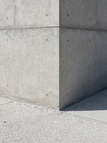 Close-up of a finished architectural concrete wall meeting a clean gravel pathway, sharp shadows, overcast light.