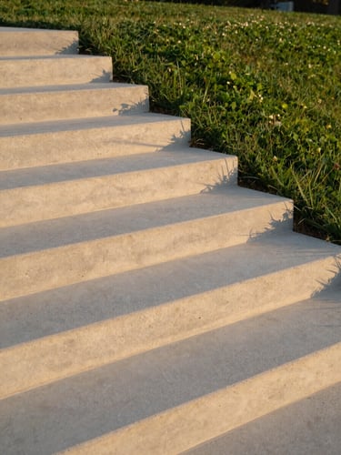 Low-angle golden hour shot of pristine board-formed concrete steps cascading into a manicured luxury lawn, architectural concrete texture highlighted by shadows