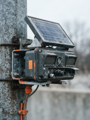 Macro close-up of a rugged solar-powered air quality sensor mounted on a steel utility pole, overcast daylight, desaturated cool tones with safety orange accents, 35mm.