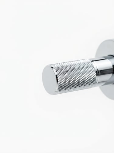 Close-up of a high-quality, polished chrome faucet handle, sharp focus on the knurled texture, bright studio light, seamless white backdrop, 50mm lens. Panoramic 21:9 frame, handle to the right third.